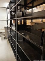 Photo of long row of black metal shelving units with multiple shelves, showing length and shelving depth.