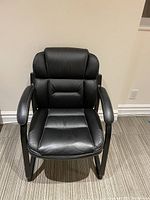 Black office chair photographed from the front showing padded seat, backrest, armrests, and sled base.