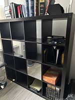 Modern black cubicle bookcase holding books and office items, showing design and condition