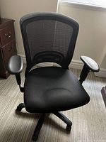 Front view of black mesh office chair showing padded seat and armrests.