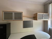 Full view of floating desk shelving unit including two wall mounted cabinets with metal framed frosted glass doors and floating shelf in between on a wall above a desk.