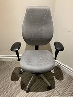 Front view of the grey desk chair showing mesh seat and backrest, black armrests, and caster wheels on metal base.
