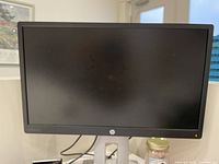 Front view of HP desktop monitor turned off showing black screen, HP logo below display, and silver stand.