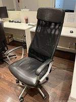 Front view of the black office chair showing faux leather seat, mesh backrest, padded armrests, and caster wheels.
