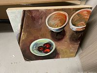 Photo of an oil painting showing a still life of two ceramic bowls and a plate with cherries on a wooden surface.