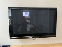 Front view of Panasonic TV mounted on wall showing screen and buttons below the screen