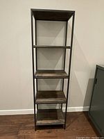 Full front view of the shelving unit showing five wooden shelves supported by a black metal frame against a plain wall.