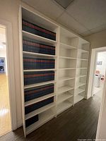 Full view of two tall white Ikea Billy bookcases with books on some shelves adjacent to a hallway