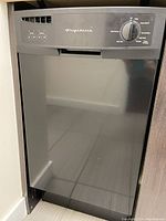 Front closed view of black Frigidaire apartment-size dishwasher showing control panel with cycle selector dial and buttons.