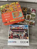 Three puzzle boxes stacked showing the front artwork of Wines of Spain & Portugal and Country Life puzzles with a third puzzle partially visible underneath.