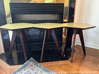 Front view of three hexagonal occasional tables with beige tops and dark wood legs arranged in front of a fireplace.