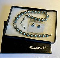 Grey bead necklace and matching stud earrings displayed in a Shepheard's branded black jewelry box with white lining.