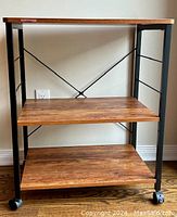 Full view of kitchen cart showing three wooden shelves and black metal frame with wheels