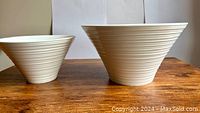 Two white ceramic Maxwell & Williams bowls on a wooden table, showing their size difference and ribbed exterior design.