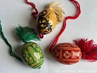 Top view of the three wooden Easter eggs displaying their distinct hand-painted floral and geometric designs and attached tassels.