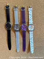 Four Swatch Skin watches displayed in a row on corkboard