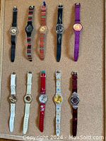 Ten women's Swatch watches arranged in two rows on cork board