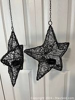 Photo of two black wire star-shaped hanging candle holders, each with a small platform for holding a candle, hanging against a white door.