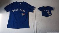 Both jerseys laid flat: one adult XL and one kids 12 month, blue with White Jays logo and text