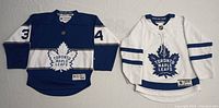 Front view of two hockey jerseys, blue and white, both Toronto Maple Leafs with logos and number 34 on blue jersey.