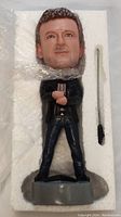 Front view of Alan Frew bobblehead in white foam packaging with separated accessory wrapped in bubble wrap.