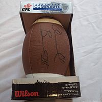 Front view of football in original CFL Ultimate Composite box showing Wilson branding and part of the factory packaging. Signature visible on brown textured composite.
