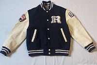Front view of vintage Roots letterman jacket showing navy blue wool body and off-white leather sleeves.