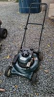 Side angle showing full mower with handle and wheels on gravel surface