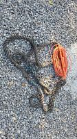 Photo of an orange extension cord coiled neatly next to a loosely coiled thick rope laid on gravel.