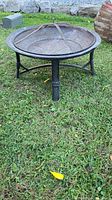 Front angled view of a round metal fire pit with mesh cover on grass.