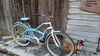 Wide side view of the light blue and white ladies cruiser bicycle parked on pavement near wooden fence.