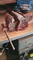 Heavy-duty cast iron bench vise on a workshop bench, showing rust and dirt, marked Number 3.