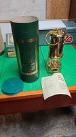 Miner's lamp along with its original green packaging box and instruction leaflet arranged on green surface.
