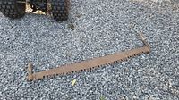 Full view of vintage two-man crosscut saw lying on gravel, showing entire blade and handles.