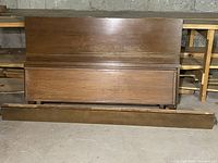 Wooden bed frame parts including headboard and footboards stacked against wall, showing finish and wear.