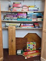 Full view of shelves with multiple board games and game accessories including Crokinole board and wooden cribbage board.