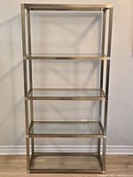 Full view of the five-tier shelving unit showing the brass frame and glass shelves.