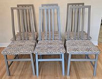Front view showing all six metal dining chairs with patterned upholstered seats and tall vertical slat backs.