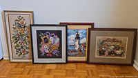 Four framed embroidery artworks displayed together on floor showing variety in themes and sizes