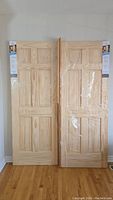 Two pine doors front view with original packaging and a stack of narrow frame boards at right