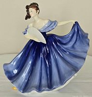 Front and partial profile view of the Royal Doulton Elaine figurine showing details of the flowing blue dress and fan.