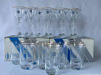 Set of 10 wine glasses with gold rim on top of 7 highball glasses also with gold rims, all displayed with original Schott Cristal packaging in background.