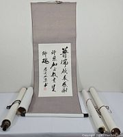 Full view of an unrolled calligraphy scroll mounted on light gray fabric with other rolled scrolls arranged around it.