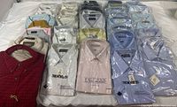 Overview of 28 collared shirts laid flat on a surface, mixed colors and packaging visible
