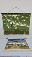 Full view of both tapestries, the green yarn sheep field hanging on the wall and the Great Potala Palace tapestry laid flat on a table.