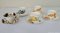 Front view of four different teacup and saucer sets showing floral designs and gold accents on porcelain.