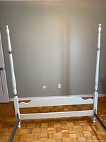 Full view of white painted wooden 4-poster headboard with turned posts, metal side rails connected to the frame, and parquet floor beneath.
