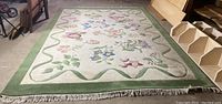 Full view of rectangular wool area rug laid flat showing floral pattern and green border with cream background.