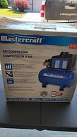 Box front showing Mastercraft branding and product image with key features noted such as 2 US gallon tank and 1/5 HP motor.