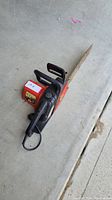 Full view of electric chain saw lying on concrete floor.